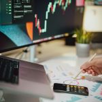 a person writing on a piece of paper next to a computer monitor