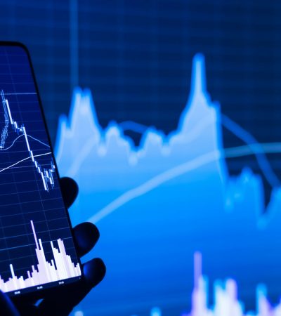 a person holding a cell phone in front of a stock chart