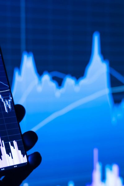 a person holding a cell phone in front of a stock chart