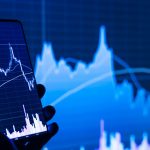 a person holding a cell phone in front of a stock chart