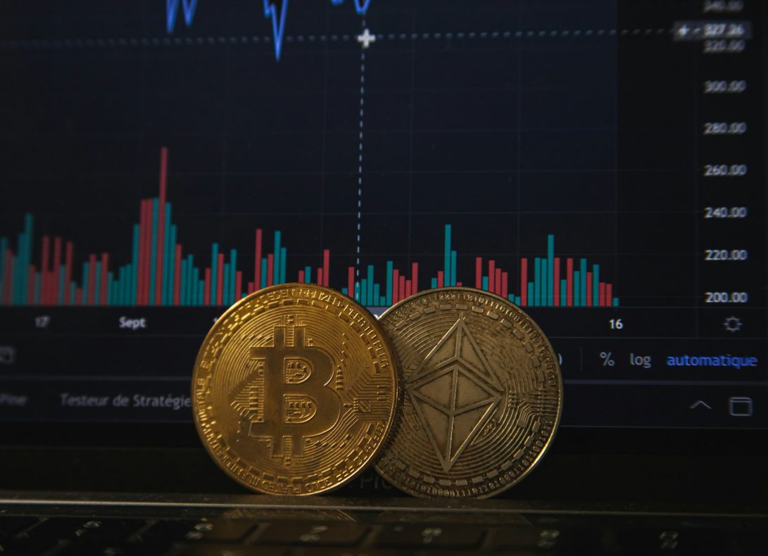 Gold Bitcoin and silver Ethereum coins resting on a laptop keyboard before a trading chart